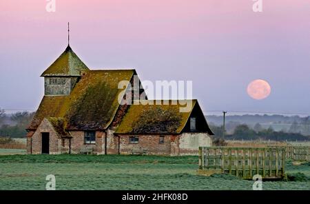 Der Mond geht hinter der St. Thomas Becket Kirche auf Romney Marsh in Fairfield, Kent, unter. Der erste Vollmond des Jahres 2022 - der Wolfmond, so die nordamerikanischen Ureinwohner - ist Montagabend. Bilddatum: Montag, 17. Januar 2022. Stockfoto