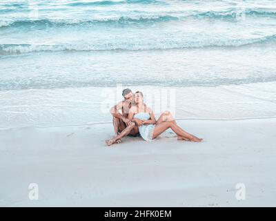 Schöner Mann und hübsche Frau sitzen am Strand Stockfoto