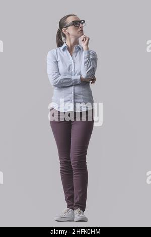 Junge Frau posiert und denkt mit der Hand am Kinn, isoliert auf grauem Hintergrund Stockfoto