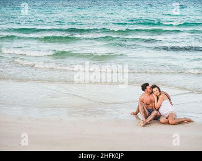 Schöner Mann und hübsche Frau sitzen am Strand Stockfoto