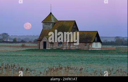 Der Mond untergeht hinter der St. Thomas Becket Kirche in Fairfield, Kent. Der erste Vollmond des Jahres 2022 - der Wolfmond, so die nordamerikanischen Ureinwohner - ist Montagabend. Bilddatum: Montag, 17. Januar 2022. Stockfoto