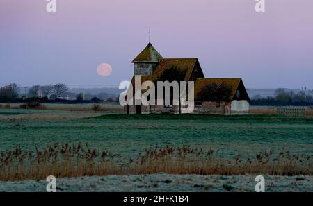 Der Mond untergeht hinter der St. Thomas Becket Kirche in Fairfield, Kent. Der erste Vollmond des Jahres 2022 - der Wolfmond, so die nordamerikanischen Ureinwohner - ist Montagabend. Bilddatum: Montag, 17. Januar 2022. Stockfoto