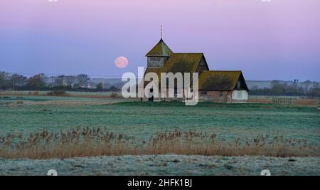 Der Mond untergeht hinter der St. Thomas Becket Kirche in Fairfield, Kent. Der erste Vollmond des Jahres 2022 - der Wolfmond, so die nordamerikanischen Ureinwohner - ist Montagabend. Bilddatum: Montag, 17. Januar 2022. Stockfoto