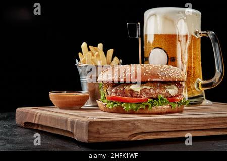 Burger mit Rinderpastete, Blauschimmelkäse, karamellisierten Zwiebeln, frischem Gemüse, serviert mit hellem Lagerbier, Pommes frites und Sauce Stockfoto