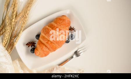 Gebackenes Croissant mit frischen Blaubeeren auf einem weißen Teller mit Kopierfläche auf weißem Hintergrund. Draufsicht Stockfoto