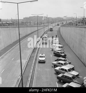 A500, Newcastle-under-Lyme, Staffordshire, 27/06/1973. Ein Polizeiauto, das am offiziellen Eröffnungstag am A500 eine Reihe von Reisebussen entlang der Potteries D Road führt und an einer Reihe geparkter Autos auf der Fahrbahn vorbeifährt. Dieses Foto ist Teil einer Serie, die die Eröffnungszeremonie für eine 6km Strecke der Potteries D Road oder Stoke D Road auf der A500 zeigt, die von Laings Highways Branch gebaut wurde. Stockfoto