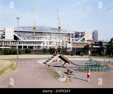 National Indoor Arena, King Edwards Road, Birmingham, c Juli 1990. Ein Blick auf die National Indoor Arena in Birmingham während der Bauarbeiten, aufgenommen aus dem Westen, mit zwei Kindern auf einem Spielplatz im Vordergrund. I/N wird neben diesem Bild in Laings Negativregister aufgezeichnet, was bedeutet, dass es sich um ein Internegativ handelt. Es scheint im Juli 1990 vom Original kopiert worden zu sein und wurde wahrscheinlich kurz vorher aufgenommen. Das Bild wurde von Allan Sloan, einem regionalen Marketing-Manager für die Midland Division von Laing, bereitgestellt. The &#XA3;50m Entwurf und Bau des Vertrags für die National Indoor Arena (NIA) Stockfoto