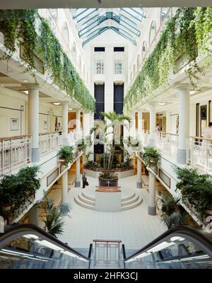 Einkaufszentrum Eldon Garden, Percy Street, Newcastle upon Tyne, 03/07/1989. Das zentrale, dreistöckige Atrium des Einkaufszentrums im Eldon Garden, von der Oberseite einer Rolltreppe aus, zeigt Palmen und Pflanzen, die von Balkonen abgesäumt sind. Das Einkaufszentrum Eldon Garden bestand aus 42 Geschäften auf 3 Stockwerken und einem Parkplatz mit 477 Stellflächen. Laing sicherte sich den &#XA3;11,5m Managementvertrag für den Bau im Jahr 1987 für Greycoat Shopping Plc. Die Arbeiten begannen im Januar 1988 und das Zentrum war ab März 1989 für die Öffentlichkeit zugänglich und im November 1989 offiziell von Prinzessin Margaret eröffnet. Die Entwicklung Stockfoto