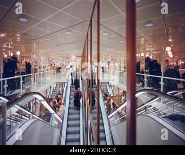 Eldon Square Shopping Centre, Newgate Street, Newcastle upon Tyne, 06/10/1987. Zwei Einkäufer, die eine Rolltreppe hinunterfahren, gefolgt von einem Sicherheitsbeamten im H&amp;M-Geschäft im Einkaufszentrum Eldon Square in Newcastle. Laing gewann den £5,2m-Vertrag zur Erweiterung des Einkaufszentrums im März 1986 zur Fertigstellung im Oktober 1987, Ein zweiter Vertrag im Januar 1987 über den Bau der Einzelhandelseinheit, die die Blackett Street verbindet und die alte mit der neuen Entwicklung verbindet, und ein dritter im Mai 1987 für Verbesserungen und Upgrades auf dem gesamten Eldon Square-Gelände. Der H&amp;M-Shop besetzt die Retail-Uni Stockfoto