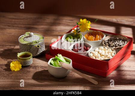 Schachtel mit Schalen kandierter Früchte und Nüsse, Teekannen und kleiner Tasse auf Holztisch, serviert für das Frühlingsfest Stockfoto