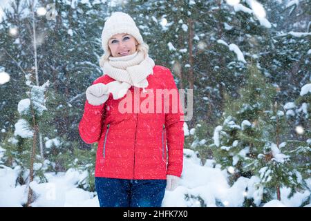 Fröhliche Frau steht im verschneiten Winterwald gegen Bäume Stockfoto