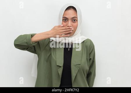 Junge asiatische Frau trägt Hijab schockiert Abdeckung Mund mit Händen für Fehler. Geheimes Konzept. Stockfoto