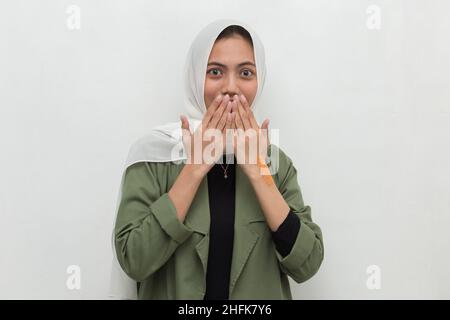 Junge asiatische Frau trägt Hijab schockiert Abdeckung Mund mit Händen für Fehler. Geheimes Konzept. Stockfoto
