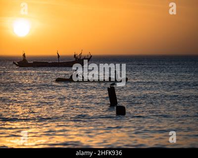 Sonnenuntergang an der Atlantikküste in Afrika und die Silhouetten eines Fischerbootes auf dem Wasser, Senegal, Afrika Stockfoto