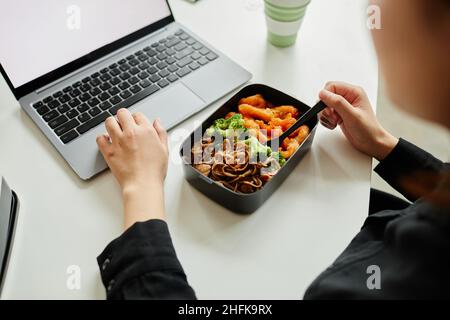 Nahaufnahme einer jungen Frau, die ein gesundes Mittagessen mit Gemüse genießt, während sie einen Laptop benutzt, Platz zum Kopieren Stockfoto