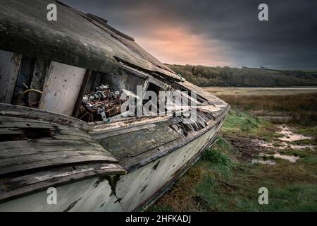 Abendlicht über dem Wrack eines alten hölzernen Motorbootes, das am Ufer des Gannel River in Newquay in Cornwall aufgegeben wurde. Stockfoto