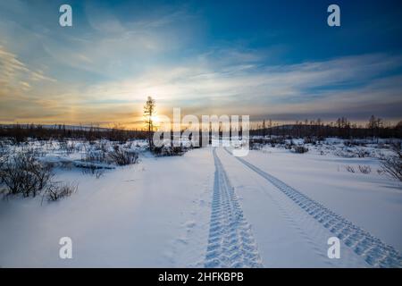 Winteruntergang und Spuren des Autos im Schnee. Südjakutien, Russland Stockfoto