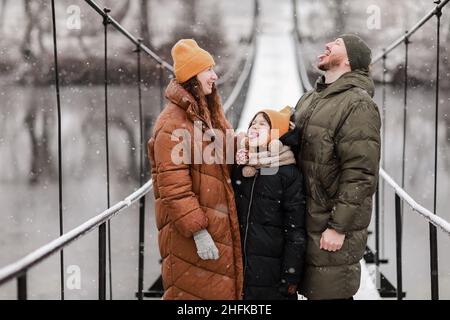 Die junge Mutter, der Vater und die kleine Tochter fangen Schneeflocken in einem schönen Winterpark während eines Schneefalls. Es schneit. Familie spielt in der Stockfoto