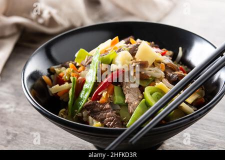Rindfleisch, Gemüse und Sesam in schwarzer Schüssel auf Holztisch Stockfoto