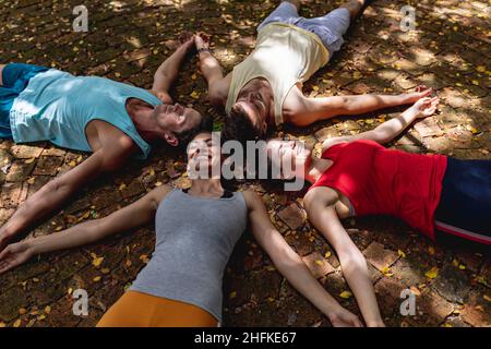 Lächelnde multirassische männliche und weibliche Freunde entspannen sich zusammen mit ausgestreckten Armen auf dem Boden Stockfoto