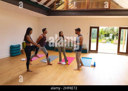 Multirassische männliche und weibliche Freunde sprechen während der Aufwärm-Übung im Yoga-Studio Stockfoto
