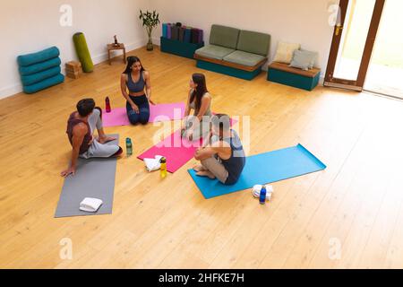 High-Angle-Ansicht von multirassischen Freunden, die diskutieren, während sie auf Übungsmatten im Yoga-Studio sitzen Stockfoto