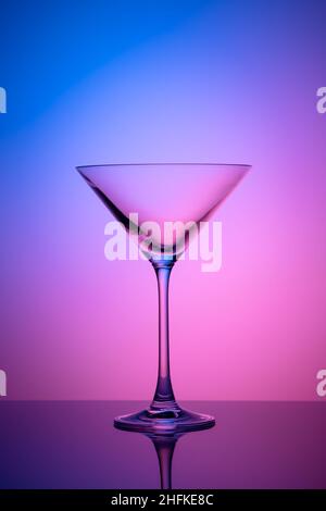 Leeres martini-Glas auf einem rosa und blauen Neonhintergrund. Alkoholgetränk, Cocktailparty-Konzept. Transparente Silhouette, Lichteffekt. Nachtbar Stockfoto