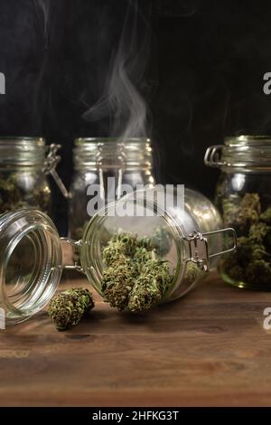 Vertikale Aufnahme von Vorratsgläsern, gefüllt mit Cannabisknospen, in einer Rauchwolke. Stockfoto