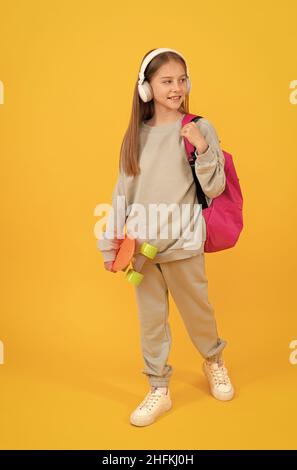 Happy teen Mädchen Kind mit Schulrucksack und Penny Board hören Musik in Kopfhörer, Schulzeit. Stockfoto