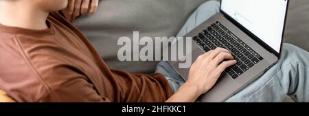 Technologiekonzept der Mann, der sich auf eine Brille stützt und sich dabei auf den Bildschirm des Laptops konzentriert, lehnt sich auf das Dunkelgelb. Stockfoto