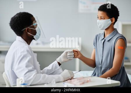 Porträt eines afroamerikanischen Teenagers, das nach einer Impfung gegen Covid-19 mit dem Arzt Fäuste anstößt Stockfoto