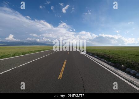 Leere gerade Asphaltstraße durch grüne Grasebene. Auf dem Weg zum weiten Horizont und weißen Wolken blauen Himmel. Weitwinkel Stockfoto