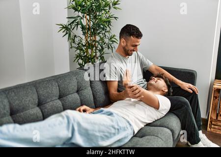 Zwei hispanische Männer, die zu Hause lächeln und selbstbewusst auf dem Sofa sitzen Stockfoto