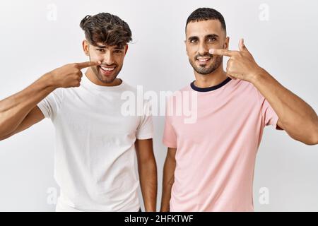 Junge schwule Paar steht über isolierten Hintergrund zeigt mit der Hand Finger auf Gesicht und Nase, lächelnd fröhlich. Beauty-Konzept Stockfoto