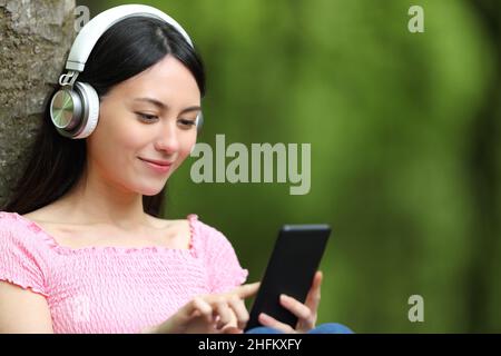 Asiatische Frau, die Musik hört und ihr Smartphone in einem Park hört Stockfoto
