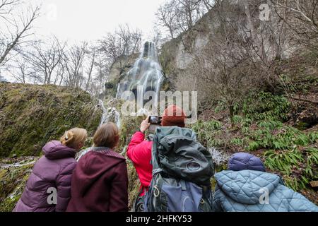 Bad Urach, Deutschland. 16th Januar 2022. Wanderer stehen unter dem Wasserfall bei Bad Urach. Der Urach-Wasserfall gehört zu den Sehenswürdigkeiten des UNESCO-Weltgeoparks Schwäbische Alb und des von der UNESCO anerkannten Biosphärenreservats Schwäbische Alb. Quelle: Thomas Warnack/dpa/Alamy Live News Stockfoto