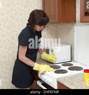 Hausfrau Frau in einem blauen Kleid und gelben Gummihandschuhe reinigt die Küche, wäscht den Gasherd. Stockfoto