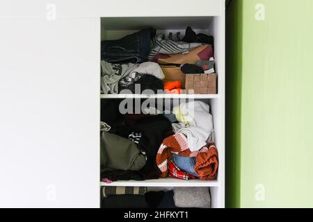 Unordnung im Kleiderschrank mit bunten Kleidern. Verschiedene Kleider auf ein weißes Regal geworfen Stockfoto