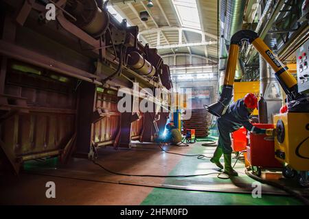 Ekibastuz, Kasachstan - 28. Mai 2012: Werkstatt für Eisenbahnwaggons. Zwei Schweißer bereiten sich auf die Arbeit vor. Wagen links, Lüftungsrohr rechts. Stockfoto