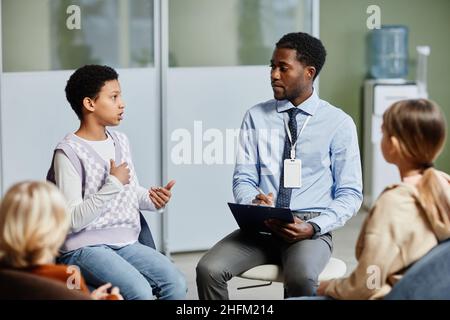 Porträt eines jungen afroamerikanischen Therapeuten, der eine Unterstützungsgruppe für Kinder mit einem Teenager-Mädchen leitet Stockfoto