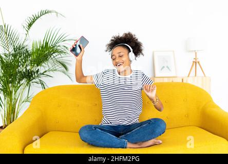 Glückliche junge Frau, die zu Hause Musik auf dem Handy hört Stockfoto