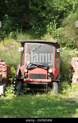 Das verlassene Wrack eines selbstgemachten Traktors, der im Garten steht, überwuchert mit Pflanzen. Stockfoto