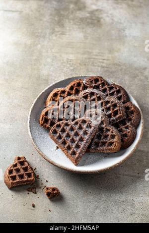 Schokoladenwaffeln in Form eines Herzens, die mit Puderzucker auf dem Teller auf texturiertem Hintergrund bestreut sind. Konzept für den valentinstag Stockfoto