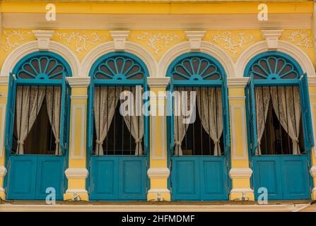 Reihe von dekorativen exotischen Osttüren oder Fenstern auf einem Gebäude auf phuket in thailand. Vorhänge öffnen sich in Bogenfenstern in thailändischer Stadtarchitektur. Stockfoto