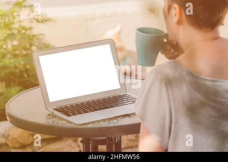 Freiberufliche digitale Nomadin, die im Urlaub arbeitet, den Laptop-Mockup-Bildschirm betrachtet und Kaffee trinkt, selektiver Fokus Stockfoto