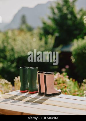 Sein und ihr Garten wellington Stiefel Austrocknen in der frühen Sommersonne auf Gartentisch - rosa grüne Gummistiefel Paar Ruhestand Lebensstil Stockfoto
