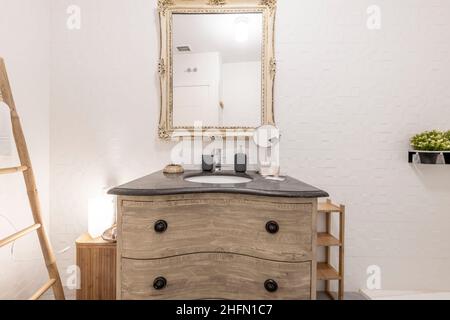 Die Toilette ist mit abgekleideten Möbeln und einem passenden quadratischen Spiegel mit einem Waschbecken aus schwarzem Marmor in der Ferienwohnung ausgestattet Stockfoto