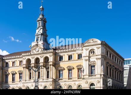 Fassade des Rathauses von Bilbao mit spanischen und baskischen Flaggen an sonnigen Tagen. Architektur im eklektischen Stil, erbaut 1892 Stockfoto