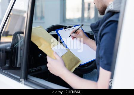 Beschnittene Ansicht des Kurierschreibens auf der Zwischenablage und das Halten des Pakets im Auto Stockfoto