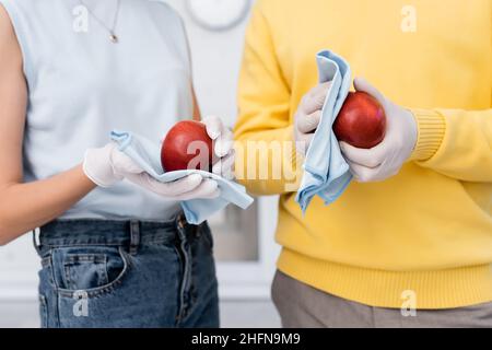 Beschnittene Ansicht eines verschwommenen Paares in Latexhandschuhen, die Äpfel in der Küche putzen Stockfoto